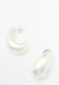 Metalen zilveren oorbellen in een abstracte, gebogen vorm met een gladde textuur. Studstijl met een veilige achterkant. Eenvoudig, modern ontwerp.