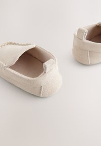Chaussons beige en daim à enfiler, avec bout ouvert, détails cousus et petites languettes en tissu au talon pour faciliter l'enfilage. Texture douce.