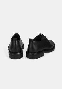 Zwarte leren schoenen met een gestructureerde oppervlakte, ronde punt en lage gestapelde hak. Beschikt over een traditionele vetersluiting en versterkte hiel.