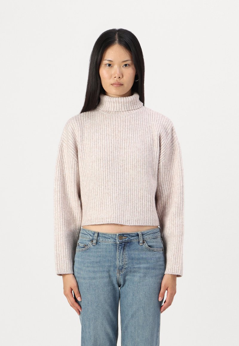 Hellrosa, gerippter Rollkragenpullover mit einem cropped Design und langen Ärmeln, kombiniert mit blauen Hochbundjeans.