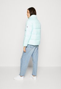 Lys blå pufferjakke med horisontal quilting, høy krage og liten logo på ermet. Kombinert med løstsittende blå jeans og hvite sneakers.
