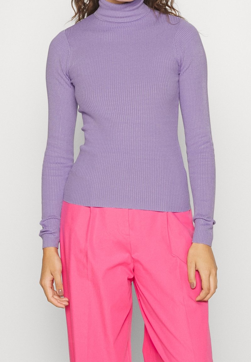 Lila ribbad polo-tröja med långa ärmar, figurnära design och slät yta; kombinerad med lysande rosa vida byxor.