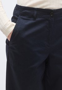 Pantaloni de culoare albastru marin, cu textură netedă, prevăzuți cu închidere cu nasturi și buzunare laterale, croială ajustată și design curat.