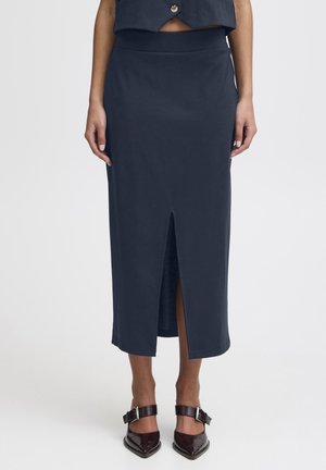 Navy enkellange rok van gladde stof, met een subtiele front split en een aansluitende tailleband. Gecombineerd met donkerbruine pumps.