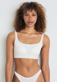 Vit mönstrad bralette med rundad halsringning och breda axelband. Har en elastisk scalloped nederkant och mjukt material.