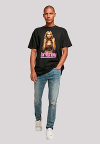 Black cotton t-shirt featuring a graphic design of a person, with the name "britney" in pink, paired with light blue distressed jeans and white sneakers.
