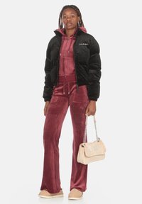 Giubbotto bomber trapuntato nero sopra un completo da ginnastica in velluto bordeaux, con dettagli in strass, e una borsa beige con catene argento.