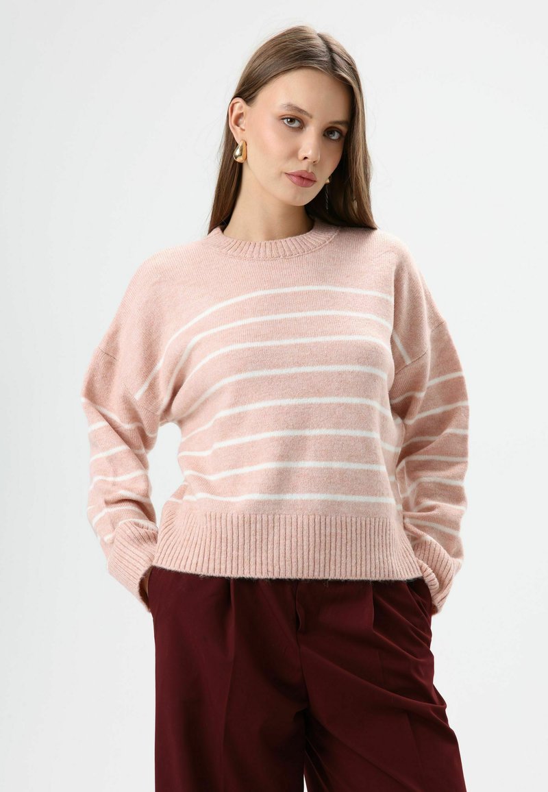 Roze gestreepte trui van zacht gebreid materiaal, met een geribbelde zoom en boord en brede mouwen. Gecombineerd met bordeauxrode broek.