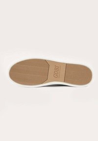 Sula på skon med ett fiskbensmönster, beige gummimaterial och vit omgivande kant; stämplat logotyp "GOBI" i mitten.