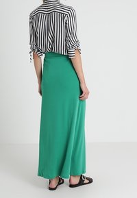 Pruhovaný černobílý triko s ohrnutými rukávy doplněné dlouhou zelenou maxi sukní. Černé sandály s kulatými detaily. Hladká textilie.