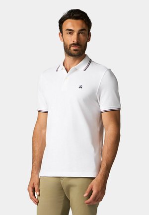 Biała koszulka polo z kołnierzykiem na dwa guziki, kontrastowymi paskami kołnierza i małym emblematem po lewej stronie klatki piersiowej. Krótkie rękawy, materiał mieszany bawełniany.