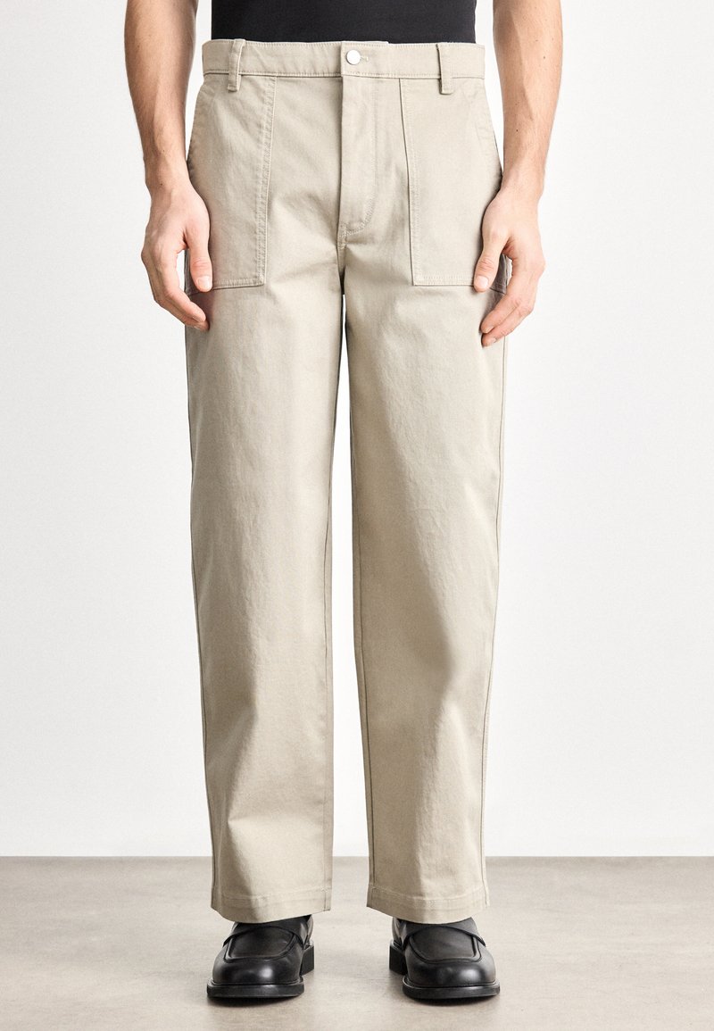 Bézs cargo nadrág egyenes szárú kivitelben, két első zsebbel, gombos záródással, és texturált pamut anyagból.