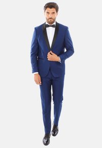 Completo da uomo blu con rever nero e chiusura a un bottone, abbinato a una camicia bianca e papillon nero. Eleganti scarpe da dress nere lucide.