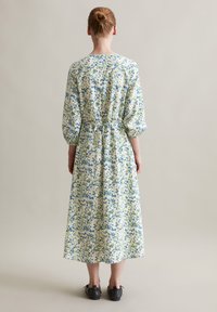 Blumiges Midikleid mit Ballonärmeln, das eine Kordelzug-Taille hat. Heller Hintergrund mit blauen und grünen Blumenmustern, weicher Stoff.