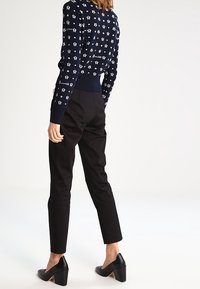 Mörkblå tröja med vita mönstrade motiv; figursydd design. Svarta skräddarsydda byxor, avsmalnande snitt. Svarta klackskor. Slät textur.