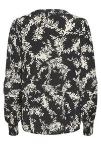 Blouse noire à motif floral blanc, manches longues, poignets élastiques et coupe décontractée. Tissu lisse avec une texture légèrement brillante.