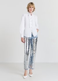 White long-sleeve shirt with ruffles and buttons at the front, paired with shiny silver sequined pants and white pointed-toe heels.