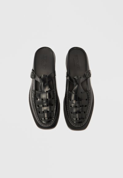 Μαύρα δερμάτινα παπούτσια χωρίς κορδόνια με υφαντό σχέδιο στο μπροστινό μέρος, στρογγυλεμένη μύτη και ρυθμιζόμενο λουράκι με αγκράφα. Επίπεδη σόλα με λεπτομέρειες ραφής.