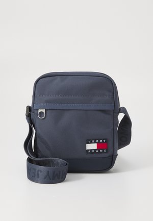 Navy blue crossbody bag made from durable fabric, featuring a logo patch, zip closure, and adjustable strap with repeating text.