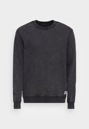 Sweat-shirt gris foncé en tissu doux et texturé avec un col rond et des poignets côtelés. Il présente une petite étiquette décorative sur l'ourlet inférieur.