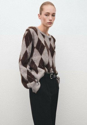 Suéter de patrón argyle en marrón y gris, en material suave, con cuello redondo y mangas sueltas, combinado con pantalones negros de cintura alta.