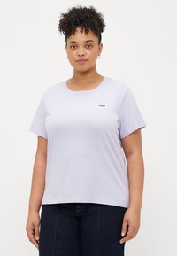 Camiseta corta de manga corta en color lila, hecha de algodón. Presenta un escote redondo y un pequeño logo rojo en el pecho. Textura suave, corte relajado.