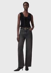 Czarny aksamitny top z krótkim rękawem i wiązanym przodem, zestawiony z wysokim stanem ciemnoszarych szerokich spodni dzwonowych oraz czarnymi botkami na obcasie.