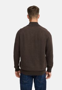 Brun strikket sweater med høj krave, ribbede manchetter og kant. Båret over blå jeans, som viser et tekstureret stof og ensfarvet design.