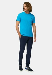 T-shirt di cotone blu con maniche corte e collo rotondo, abbinata a pantaloni slim fit blu scuro e sneakers nere con dettagli blu e bianchi.