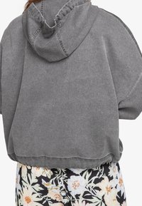 Sudadera corta gris con capucha ajustable, que presenta una textura suave y detalles de costura prominentes, combinada con pantalones de estampado floral.