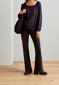 Navy long-sleeve top with a square neckline, paired with black flared jeans and chunky heeled boots. Carrying a black crocheted shoulder bag.