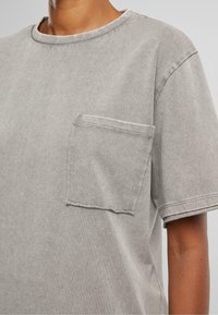 T-shirt en coton gris avec un col rond, des manches courtes et une poche poitrine. Présente une texture douce et un design décontracté.