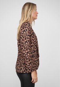 Halenka s leopardím potiskem v hnědé a černé barvě, s dlouhými rukávy a volným střihem. Hladký, lesklý materiál s přizpůsobeným siluetou.
