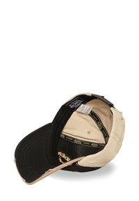 Gorra de béisbol negra y beige con visera curva, costuras visibles y etiquetas internas. Presenta acentos desgastados y correa ajustable.