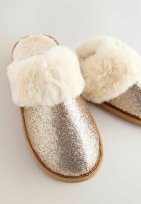Glittery gold slippers with a plush cream faux fur cuff, flat sole, and rounded shape. Textured glitter finish covers the upper.