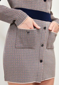 Gonna al ginocchio con motivo houndstooth nei colori blu navy, arancione e crema. Presenta bottoni in tonalità oro e tasche laterali. Tessuto texturizzato.