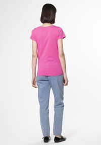 Camiseta de manga corta fucsia de algodón, combinada con jeans de mezclilla azul claro con manchas plateadas y zapatos negros.