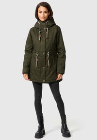 Olijfgroene parka jas met een trekkoord capuchon, voorzakken en bruine leren accenten. Voorzien van een knoopsluiting en een trekkoord in de taille.