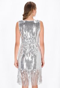 Abito di paillettes argento con un corpetto aderente, vita stretta e dettagli in frangia sull'orlo. Design senza maniche, texture lucida.