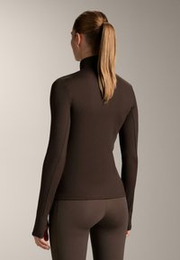 Hnedý rebrovaný top s dlhým rukávom a vysokým golierom, priliehavý strih. Tkanina má hladkú textúru a žiadne viditeľné vzory ani ozdoby.