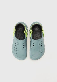 Blaue Gummi-Clogs mit grünen Akzenten, ausgestattet mit Belüftungsöffnungen, einer strukturierten Innensohle und einem gewellten Design entlang der Kanten.