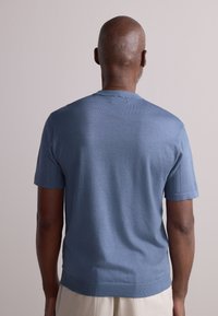 Pull en tricot à manches courtes de couleur bleu clair, doté d'un col rond et de poignets côtelés. Texture douce et lisse avec des coutures minimales.