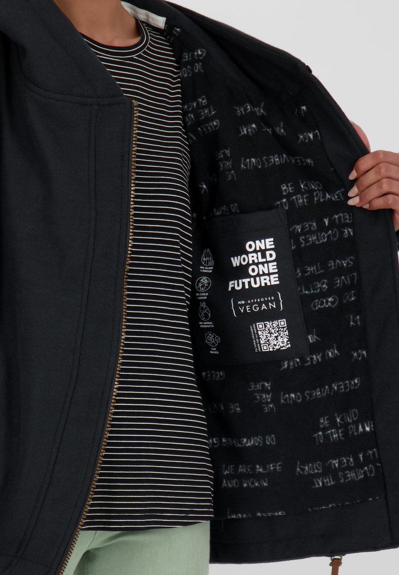 Czarna kurtka z złotym zamkiem, z wzorzystym wnętrzem z frazami oraz boczną kieszenią oznaczoną "JEDEN ŚWIAT JEDNA PRZYSZŁOŚĆ" z wegańskimi detalami.