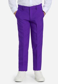 Los pantalones morados a medida presentan un diseño de pierna recta con plisados frontales. Se llevan con una camisa blanca de botones y zapatillas blancas.