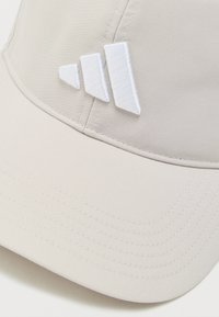 Μπεζ καπέλο μπέιζμπολ με τρεις λευκές κεντητές κάθετες ρίγες στην εμπρόσθια επιφάνεια πάνω από την κυρτωμένη γείσο.