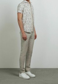 Camisa de manga corta, tipo botón, con un patrón abstracto ligero, combinada con pantalones ajustados de color claro y zapatillas blancas.