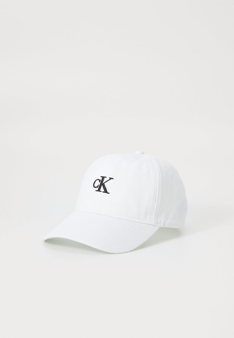 Witte baseballcap van stof, met een zwart geborduurd "cK" logo op de voorkant. Gebogen rand en verstelbare band aan de achterkant.
