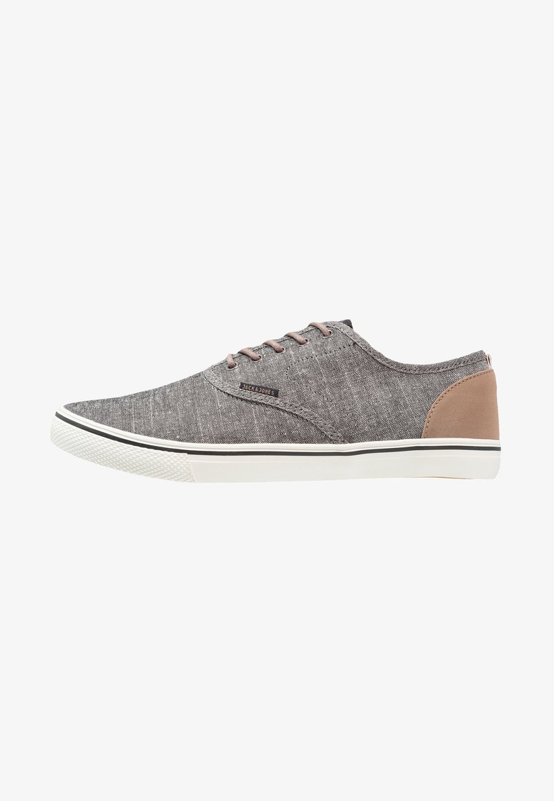 Zapatillas de tela gris con acentos beige, suela de goma blanca y cordones marrones. Presentan una parte superior texturizada y un detalle del logo en el lateral.