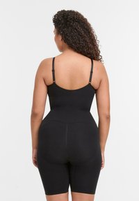 Body nero senza cuciture con spalline regolabili, caratterizzato da un design aderente e pantaloni corti fino alla coscia, texture liscia e senza cuciture visibili.
