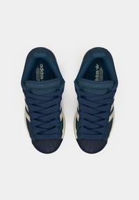 Σκούρα μπλε αθλητικά παπούτσια με λαστιχένια μύτη, με μπεζ ρίγες, υφασμένα κορδόνια και επενδεδυμένη γλώσσα για άνεση.